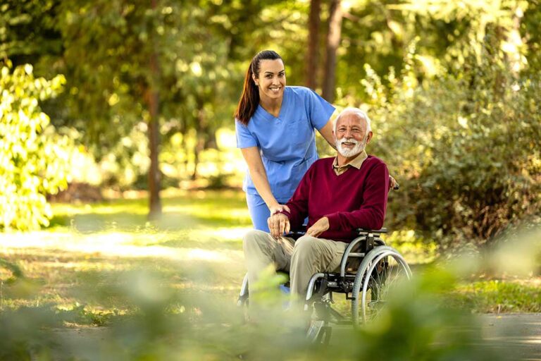 Two visitors smiling and chatting with an older adult in a bright assisted living common room.
