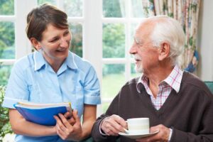 Adult daughter talking with a senior family member and staff member at a small table in a care facility.