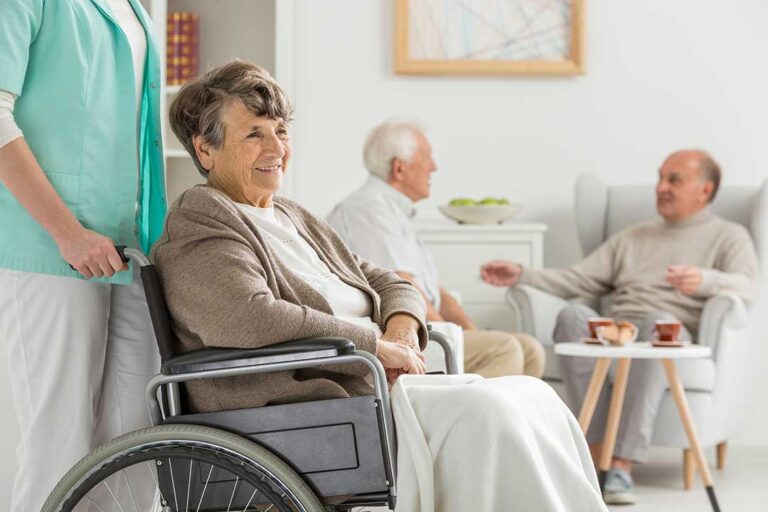 Older adult and family member organize labeled clothing and personal items in an assisted living room.